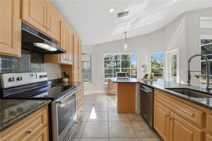 Kitchen with appliances with stainless steel finishes, dark stone countertops, light brown cabinets, under cabinet range hood, and pendant lighting