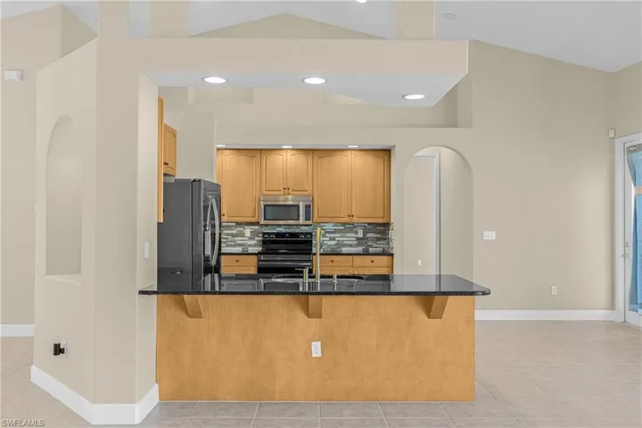 Kitchen with arched walkways, a peninsula, dark stone countertops, backsplash, and a kitchen bar