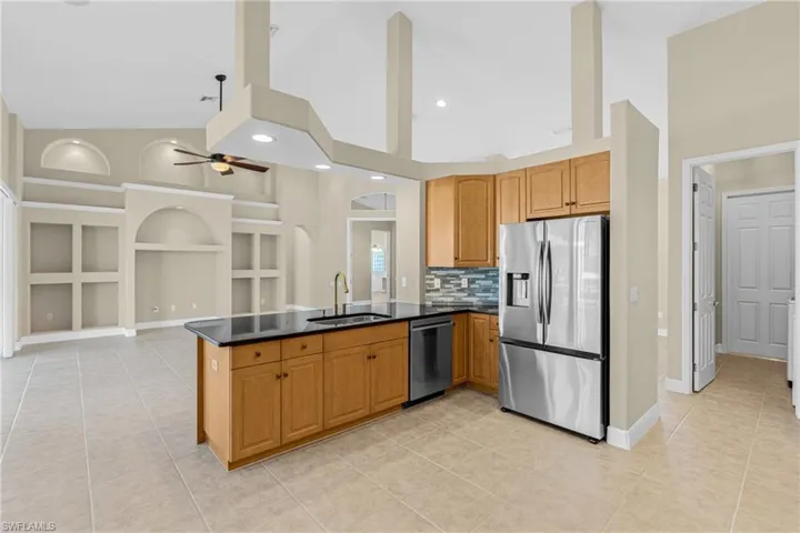 Kitchen with high vaulted ceiling, appliances with stainless steel finishes, light tile patterned flooring, backsplash, and dark stone countertops