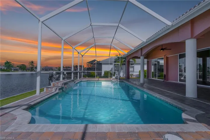 Pool at dusk featuring glass enclosure, a sunroom, a water view, and an outdoor pool