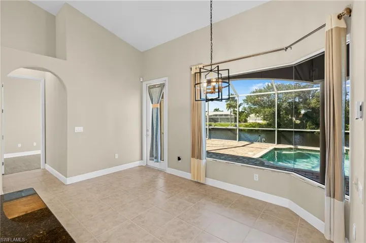 Unfurnished dining area featuring a water view, arched walkways, light tile patterned floors, lofted ceiling, and a sunroom