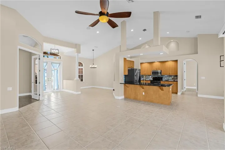 Kitchen featuring french doors, open floor plan, decorative backsplash, light tile patterned floors, and a kitchen breakfast bar