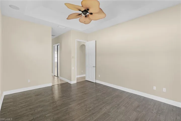 Empty room with dark wood finished floors, a tray ceiling, a ceiling fan, and arched walkways