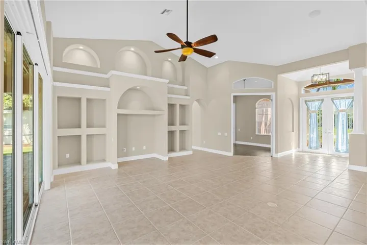 Unfurnished living room with built in shelves, plenty of natural light, light tile patterned floors, a ceiling fan, and high vaulted ceiling