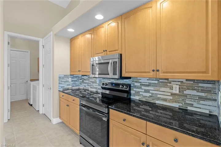 Kitchen featuring stainless steel range with electric cooktop, decorative backsplash, dark stone countertops, recessed lighting, and light tile patterned flooring