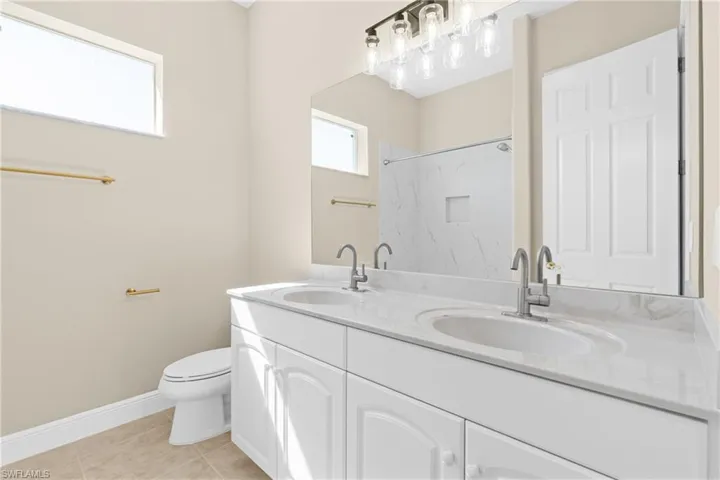 Bathroom with a marble finish shower, double vanity, and light tile patterned floors