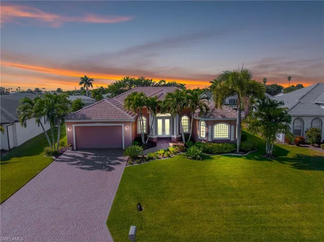 Twilight photo featuring stucco siding, a front yard, decorative driveway, and a tiled roof