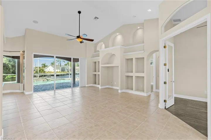 Unfurnished living room with built in features, high vaulted ceiling, light tile patterned floors, a ceiling fan, and a sunroom