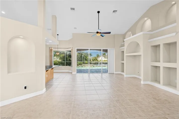 Unfurnished living room with built in shelves, high vaulted ceiling, light tile patterned floors, ceiling fan, and a sunroom