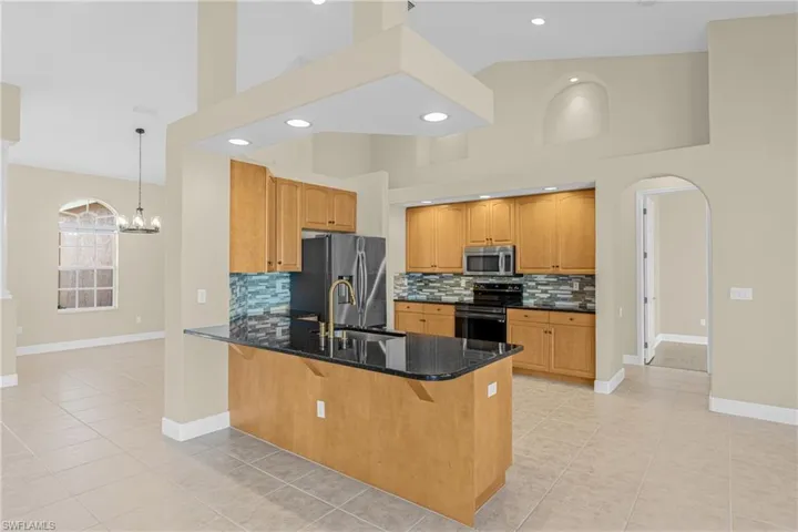 Kitchen featuring arched walkways, tasteful backsplash, dark stone counters, a high ceiling, and a peninsula
