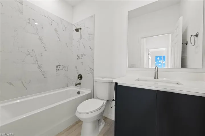 Full bathroom with hardwood / wood-style flooring, toilet, tiled shower / bath combo, and vanity