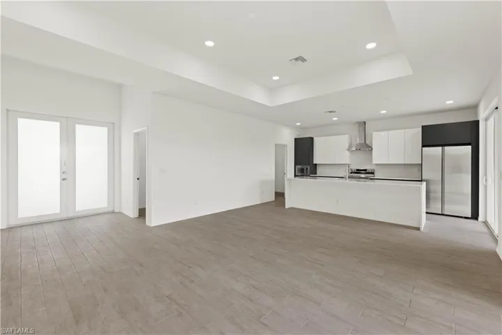 Unfurnished living room featuring sink, light hardwood / wood-style flooring, french doors, and a raised ceiling
