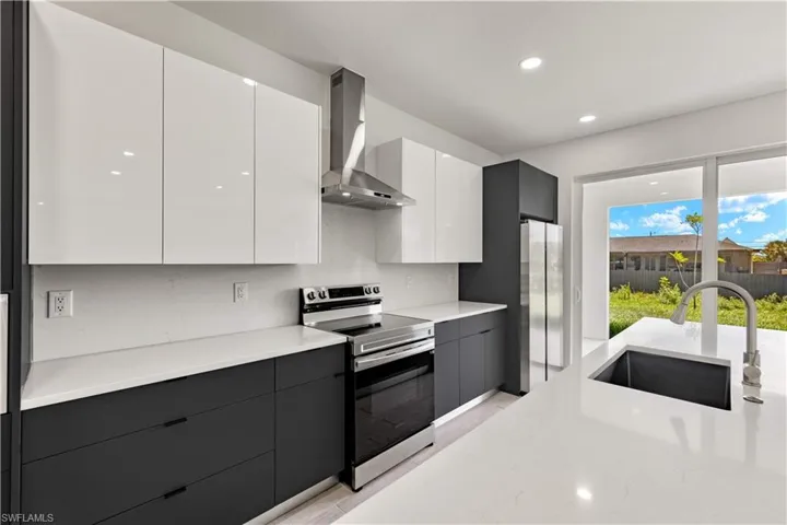 Kitchen featuring appliances with stainless steel finishes, wall chimney range hood, sink, light hardwood / wood-style floors, and white cabinetry