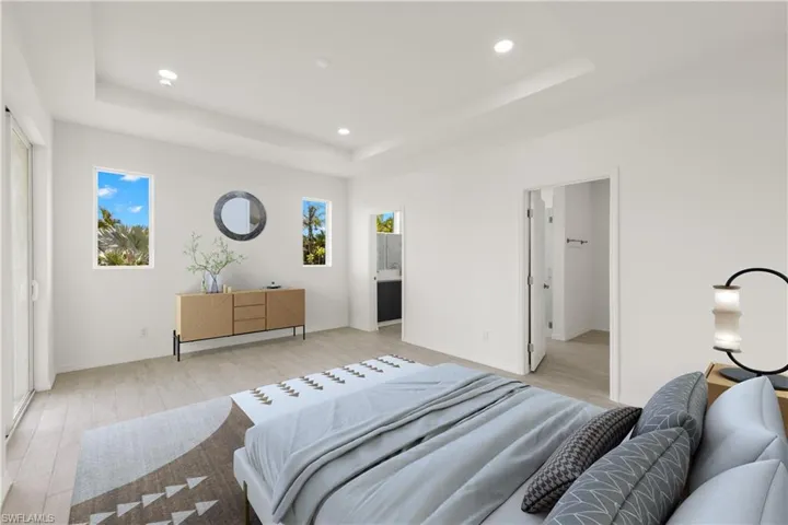 Bedroom featuring ensuite bath, a raised ceiling, and light hardwood / wood-style floors