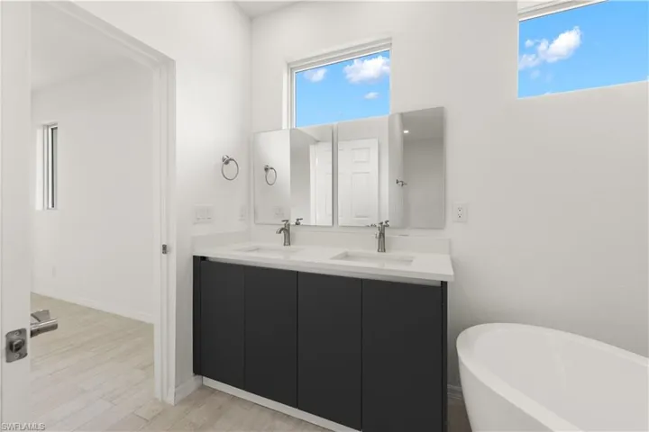 Bathroom featuring plenty of natural light, large vanity, a bath to relax in, and dual sinks