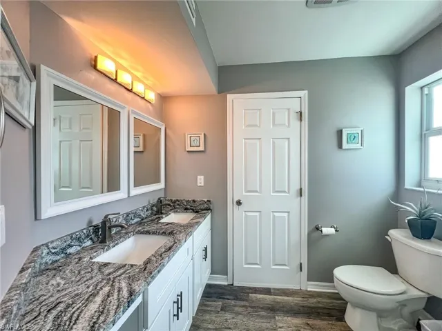 Bathroom with double vanity, a sink, toilet, and wood finished floors