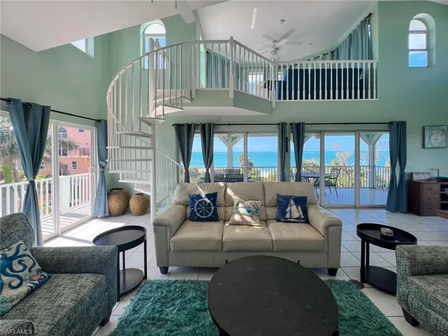 Living room with light tile patterned floors, ceiling fan, a water view, a towering ceiling, and stairway