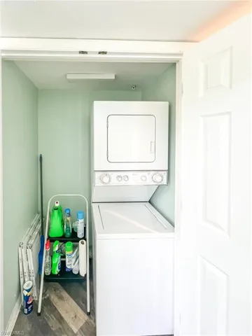 Laundry area with wood finished floors, stacked washer and clothes dryer, baseboards, and laundry area