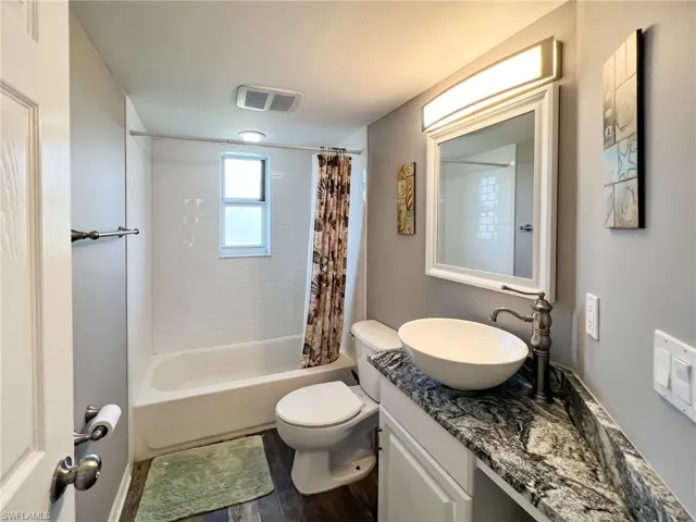 Full bathroom featuring visible vents, toilet, wood finished floors, shower / bath combo with shower curtain, and vanity