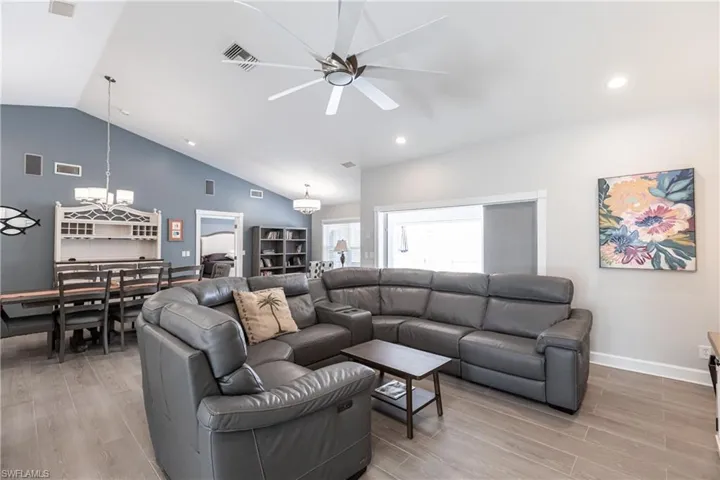 Living room with high vaulted ceiling, light wood-type flooring, and ceiling fan with notable chandelier