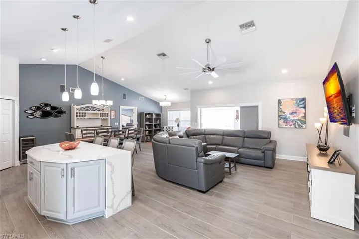 Living room featuring high vaulted ceiling, ceiling fan with notable chandelier, light hardwood / wood-style flooring, and wine cooler