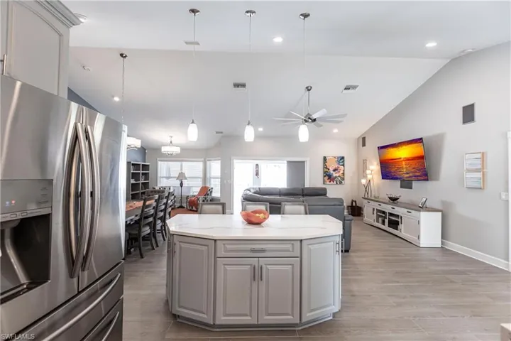 Kitchen with light hardwood / wood-style floors, vaulted ceiling, stainless steel refrigerator with ice dispenser, pendant lighting, and gray cabinetry