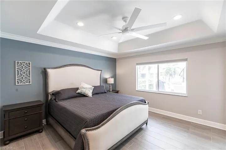 Bedroom featuring ceiling fan, a raised ceiling, light hardwood / wood-style flooring, and ornamental molding
