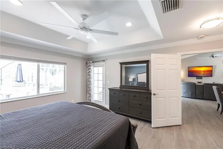 Bedroom featuring ceiling fan, a tray ceiling, crown molding, and light wood-type flooring
