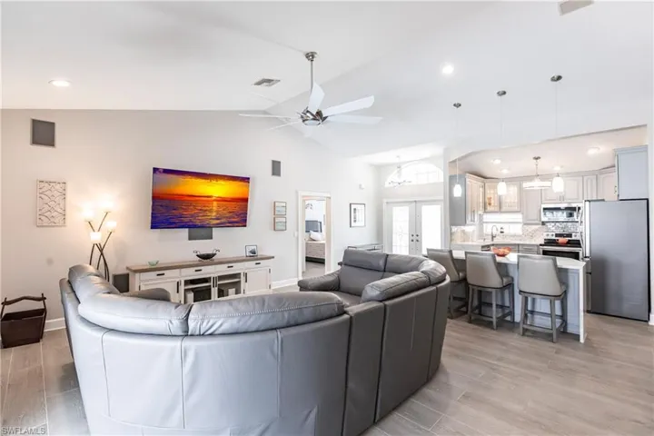 Living room with ceiling fan, light hardwood / wood-style flooring, french doors, high vaulted ceiling, and sink
