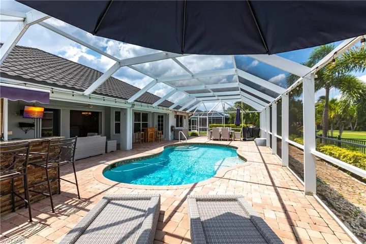 View of swimming pool with a patio area, glass enclosure, and exterior bar