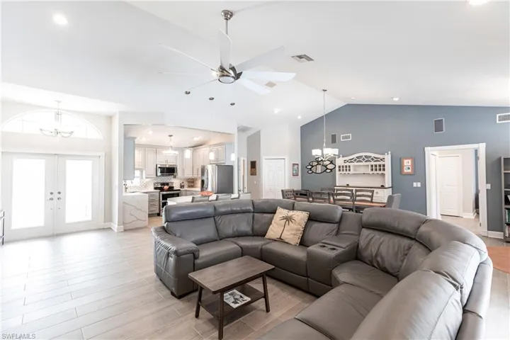 Living room featuring high vaulted ceiling, ceiling fan with notable chandelier, french doors, and light hardwood / wood-style floors