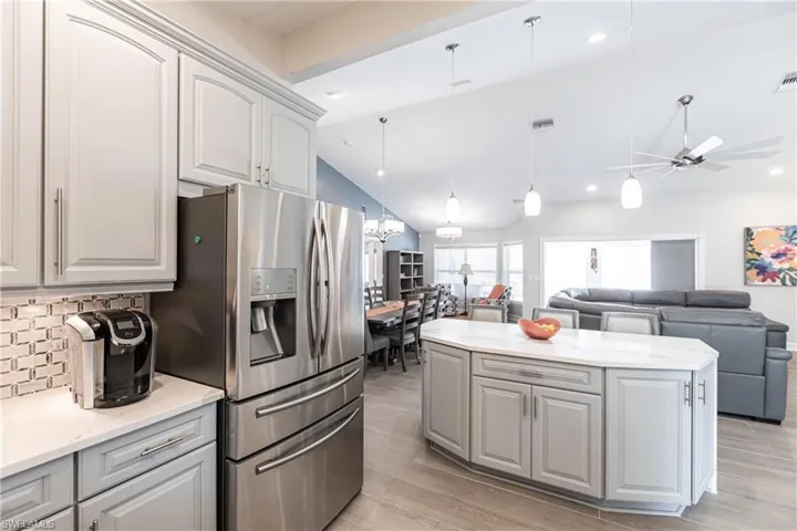 Kitchen with light hardwood / wood-style flooring, ceiling fan with notable chandelier, backsplash, hanging light fixtures, and stainless steel fridge
