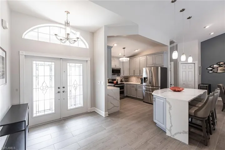 Foyer entrance featuring lofted ceiling, french doors, light wood-type flooring, and a chandelier