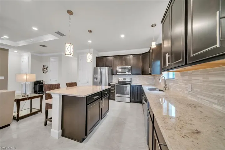 Kitchen featuring a kitchen bar, hanging light fixtures, light stone counters, appliances with stainless steel finishes, and a kitchen island