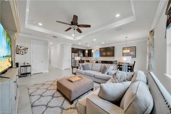 Living room with a raised ceiling, recessed lighting, a ceiling fan, and crown molding