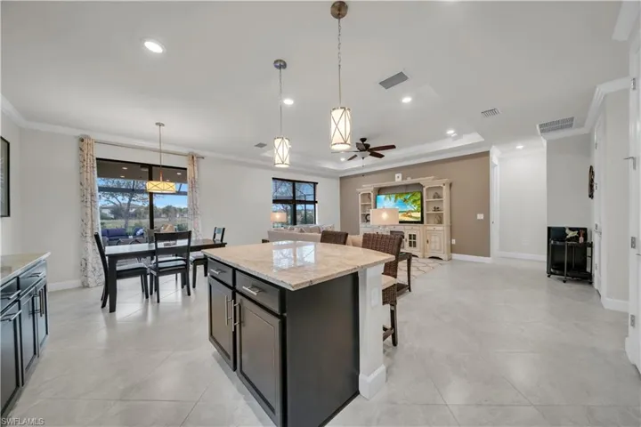 Kitchen with a breakfast bar area, crown molding, light stone counters, pendant lighting, and a kitchen island