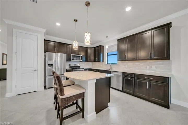 Kitchen featuring dark brown cabinetry, appliances with stainless steel finishes, ornamental molding, a breakfast bar area, and light stone countertops