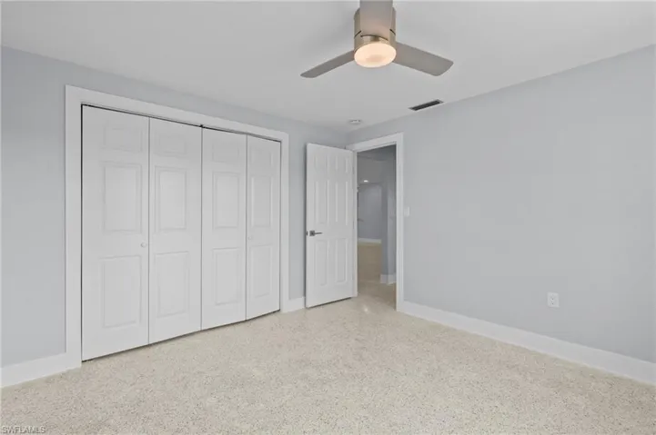 Unfurnished bedroom featuring a closet, speckled floor, a ceiling fan, visible vents, and baseboards. Virtually edited photo.