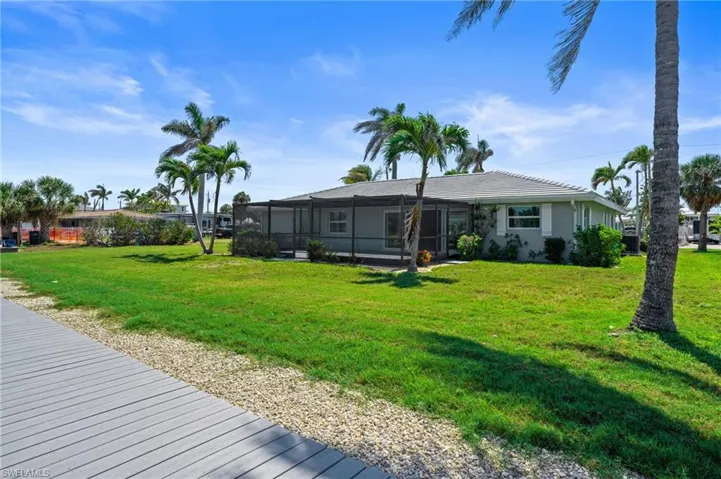 Exterior photo of back of home with screened in lanai and landscaping. Virtually edited photo.