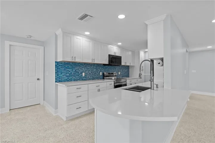Kitchen with a sink, electric stove, black microwave, and white cabinetry blue backsplash / virtually edited photo.