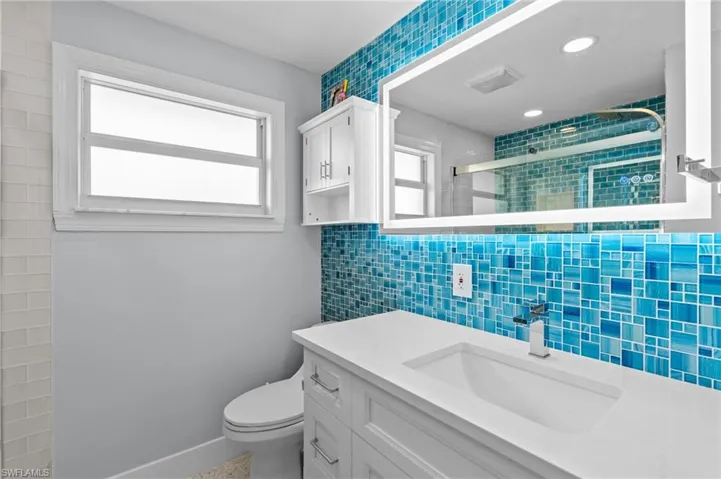 Full bathroom featuring toilet, tile walls, a wealth of natural light, and a stall shower/ virtually edited photo.