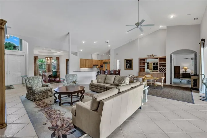 Living room featuring high vaulted ceiling, light tile patterned flooring, and ceiling fan with notable chandelier