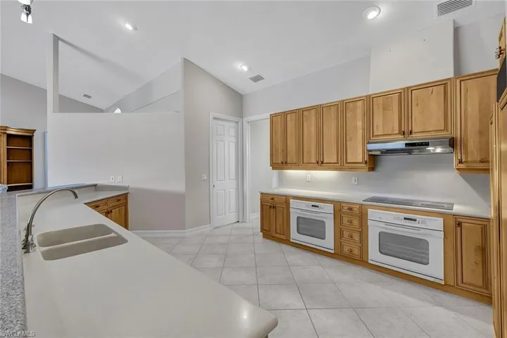 Kitchen featuring black electric stovetop, sink, light tile patterned floors, and white oven