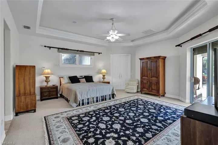Carpeted bedroom with ceiling fan, a tray ceiling, a closet, and ornamental molding