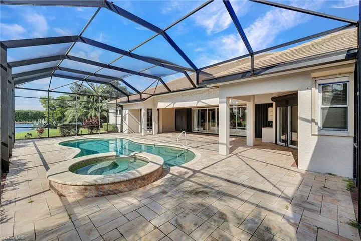 View of pool with glass enclosure, a patio, and an in ground hot tub