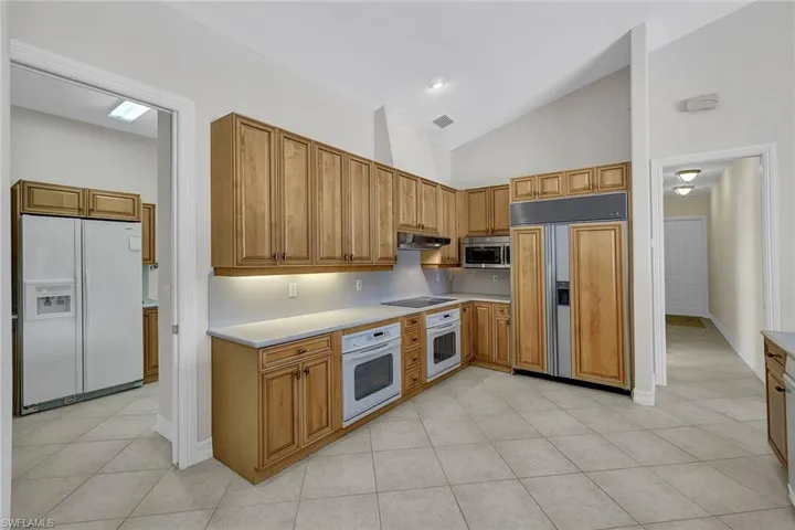 Kitchen featuring light tile patterned flooring, high vaulted ceiling, and white appliances