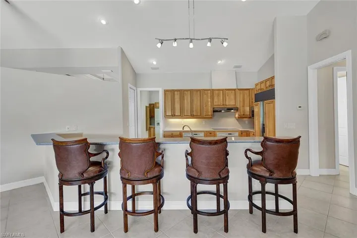 Kitchen with kitchen peninsula, rail lighting, light tile patterned flooring, a breakfast bar, and paneled built in fridge