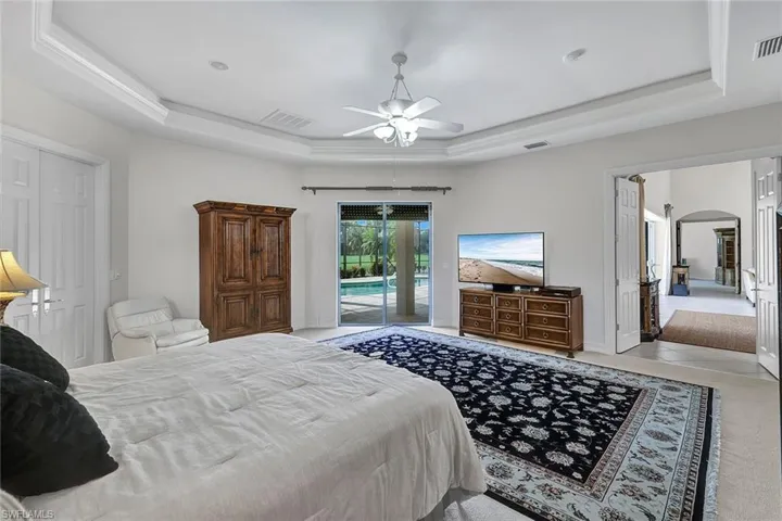 Bedroom featuring ceiling fan, a tray ceiling, light carpet, and access to outside