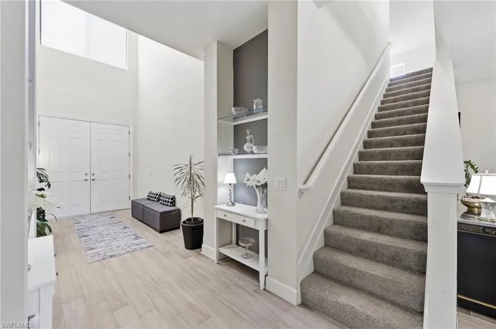Two-story foyer featuring double entry doors, natural light , wood tile flooring, a carpeted staircase, and built-in shelving with glass accents