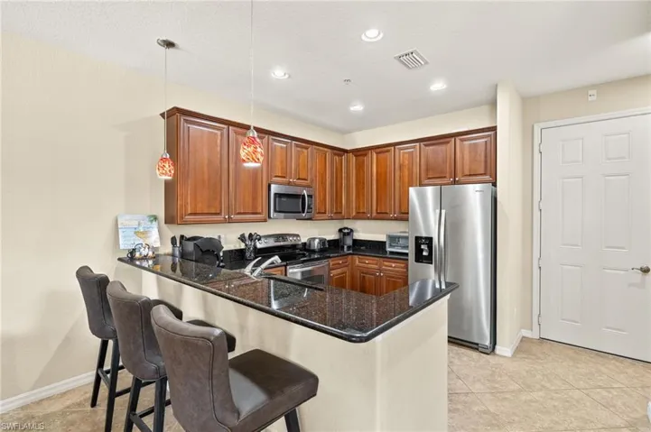 Kitchen featuring stainless steel appliances, a peninsula, dark stone counters, baseboards, and a breakfast bar